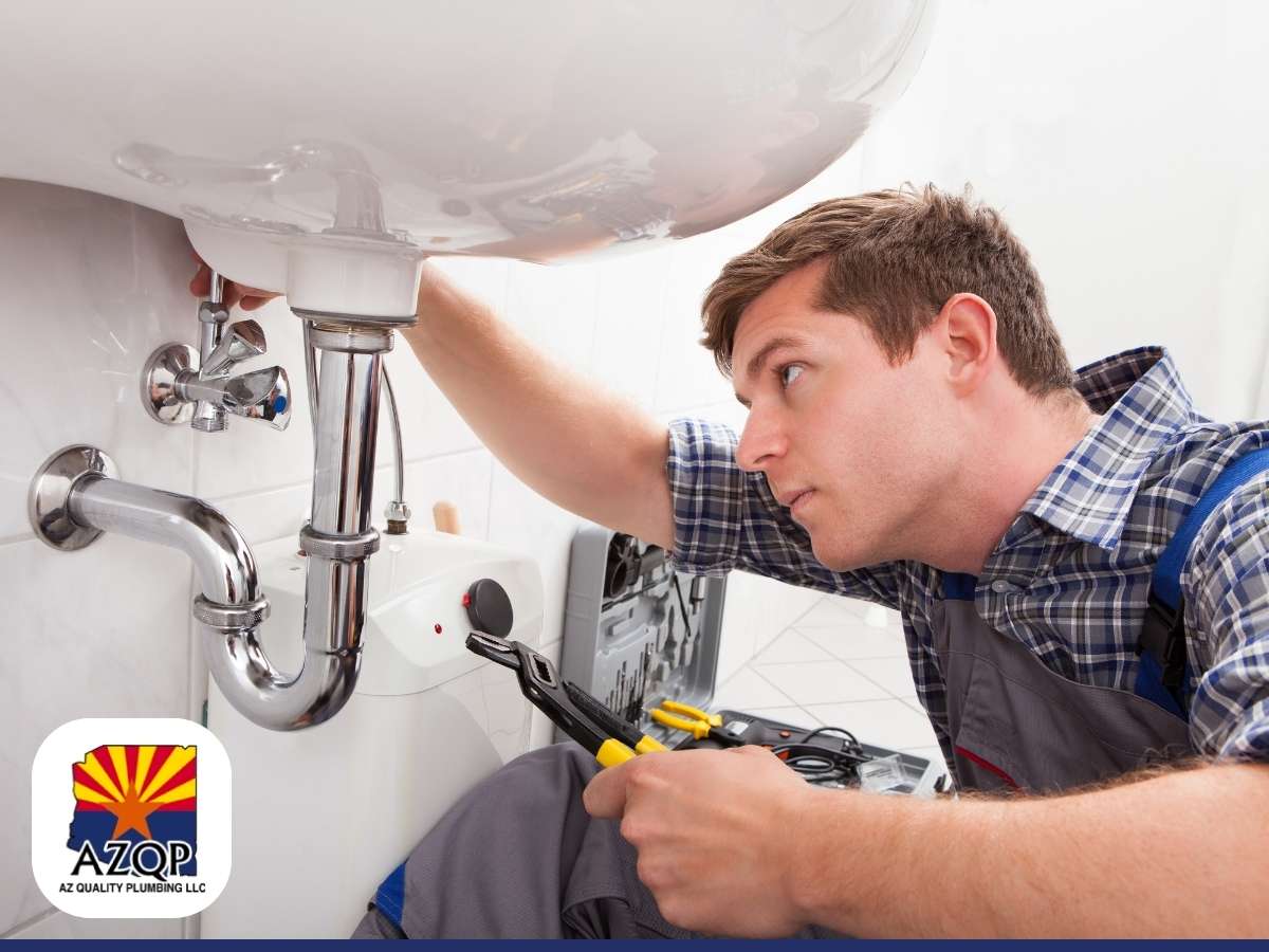 A plumber inspects a leaking water heater beneath a sink with tools in hand