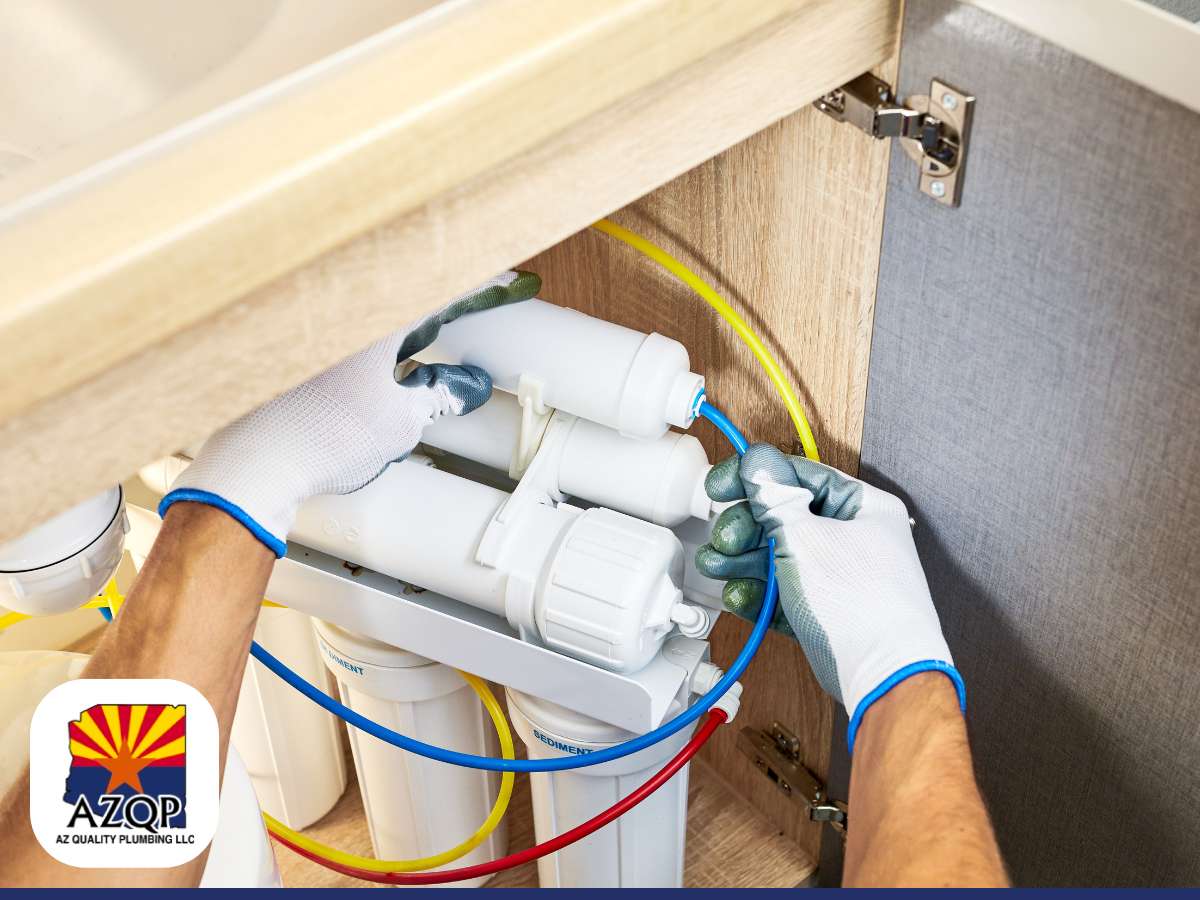 A professional plumber working on a water treatment installation under a kitchen sink, connecting pipes and filters.