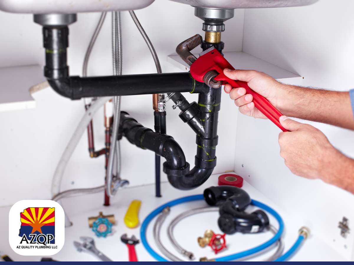 Plumber repiping under a sink as part of upgrading a home's plumbing system, with tools and pipes visible